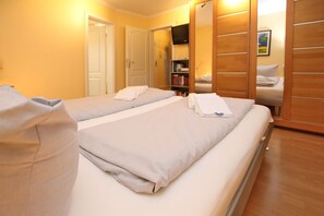 A hotel room with two beds, a wardrobe, a bookshelf, and a television.