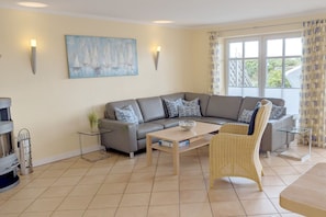 A modern living room with a grey sofa, a glass coffee table, a wicker chair, and a painting of sailboats.