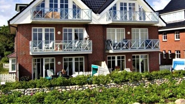 Een huis met twee verdiepingen, een balkon op de bovenverdieping, een bakstenen gevel en een stenen fundering.