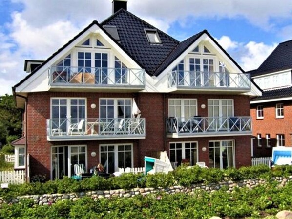 A two-story house with a balcony on the upper floor, a brick exterior, and a stone foundation.