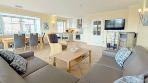 Een moderne woonkamer met een bank, eettafel, stoelen en een keukenhoek, inclusief een televisie en speakers.