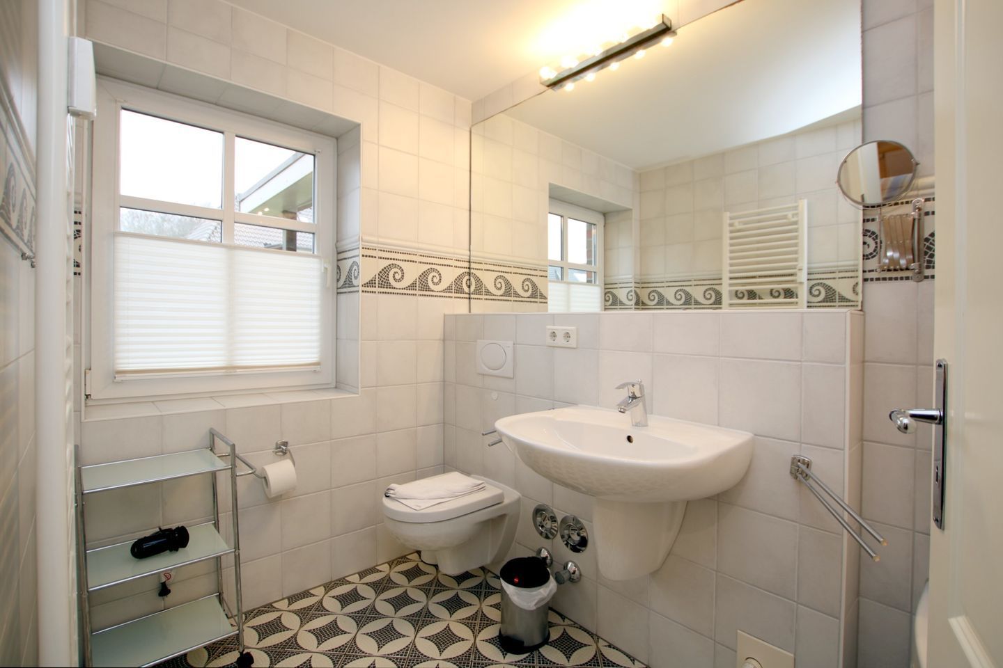 A bathroom with a toilet, sink, mirror, and patterned floor tiles.