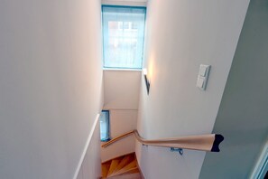 A narrow stairway with a window at the top, a handrail, and a light switch on the wall.