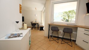 A compact kitchen with a dining area, a window with a view, and a radiator. - Osterstraße 1, Whg. 2, Haus Flora - Apartment in Wyk/ Südstrand with approx. 60m² (Wyk auf Föhr)