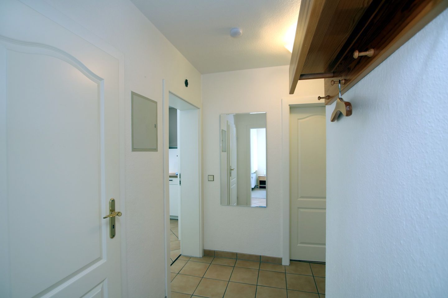 A hallway with white doors, a mirror, and a wooden ceiling beam.