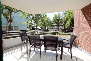 Varanda com quatro cadeiras e uma mesa, vista para uma rua com árvores e edifícios.