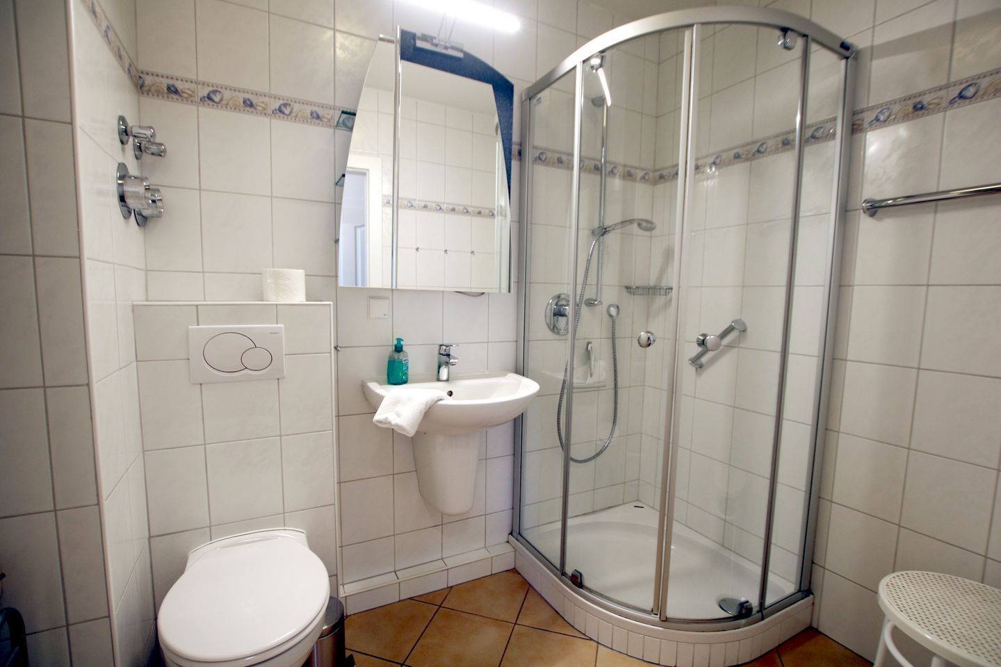 A bathroom with a toilet, sink, shower, and a mirror.