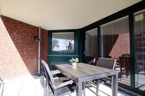 A patio with a table and chairs, a bench, a potted plant, and a view through a window.