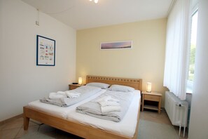Uma cama de casal com duas mesas de cabeceira, um quadro na parede e uma janela com cortinas.