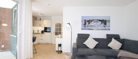 A modern living area with a grey sofa, a small round table, and a kitchen in the background.