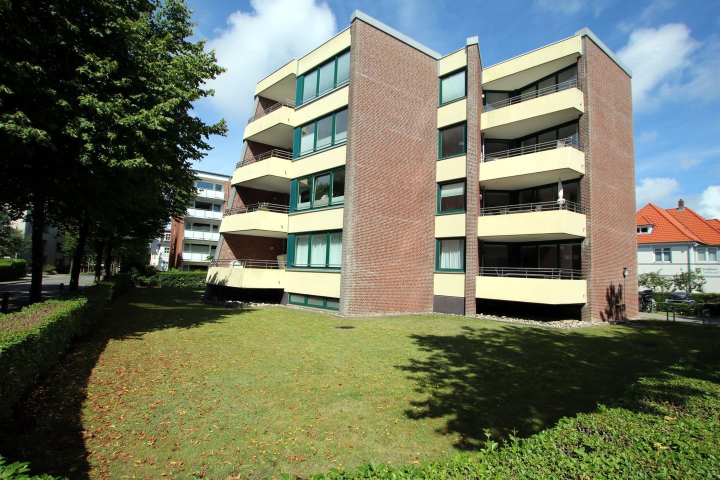 A multi-story building with balconies, a brick facade, and a grassy courtyard.