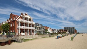 A beachfront hotel with a prominent balcony, a sandy beach, and a row of beach huts.