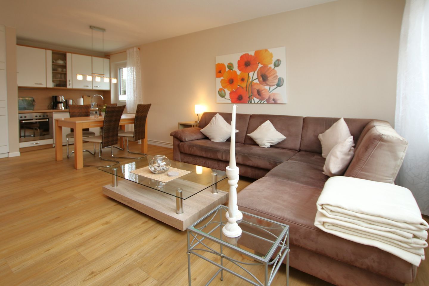 A modern living room with a glass coffee table, a brown sofa, and a dining area with a wooden table and chairs.
