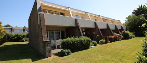 Un edificio de dos pisos con techo plano, fachada de ladrillo y un pequeño patio con mesas y sillas al aire libre.