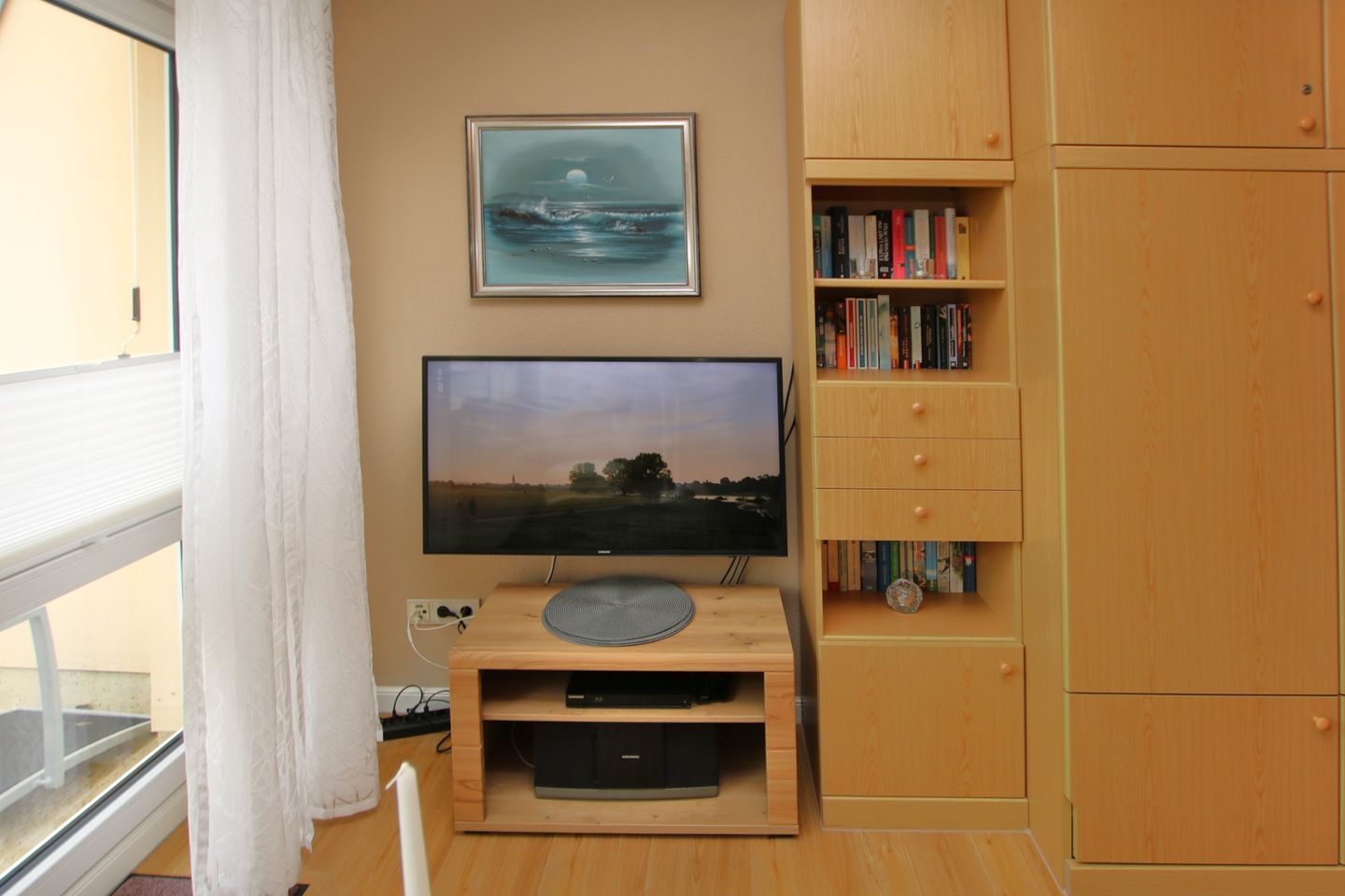 Une pièce avec un téléviseur posé sur un meuble en bois, une bibliothèque et une fenêtre avec des rideaux.
