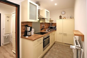 Cocina compacta con estufa, pileta y microondas. Posee una encimera de madera y un pequeño estante con utensilios de cocina.
