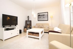 A modern living room with a flat-screen TV, a sofa, a coffee table, a fireplace, and a framed picture on the wall. - Ohl Dörp 55b, Whg. 2 - House half in Wrixum under thatched roof with 4 rooms and 140 (Wrixum)