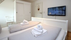 Hotellihuone, jossa on kaksi sänkyä, seinälle asennettu televisio ja vaatekaappi.