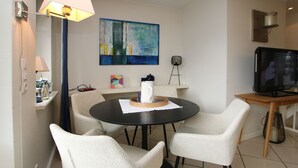 A modern living room with a round table, four chairs, a television, a painting, and a lamp.