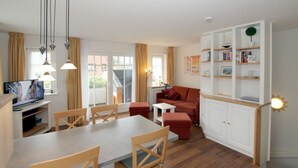A modern living room with a dining area, a red sofa, a white cabinet with shelves, and a television. - Rungholtstraße 6, Whg. 2 - Apartment with approx. 40m² (Wyk auf Föhr)