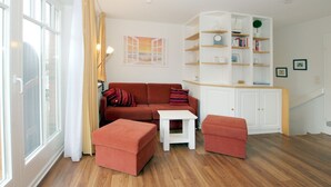 A living room with a sofa, ottomans, a small table, a white cabinet, and a bookshelf. - Rungholtstraße 6, Whg. 2 - Apartment with approx. 40m² (Wyk auf Föhr)