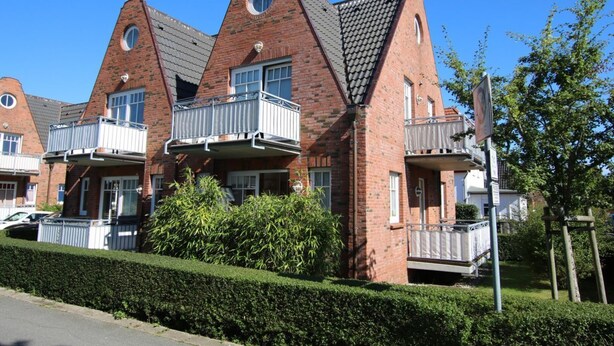 A row of brick apartment buildings with balconies, a clear sky, and a hedge in the foreground. - Rungholtstraße 6, Whg. 2 - Apartment with approx. 40m² (Wyk auf Föhr)
