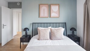 Une chambre à coucher comprenant un lit, deux tables de chevet, une tête de lit et deux tableaux abstraits accrochés au mur.