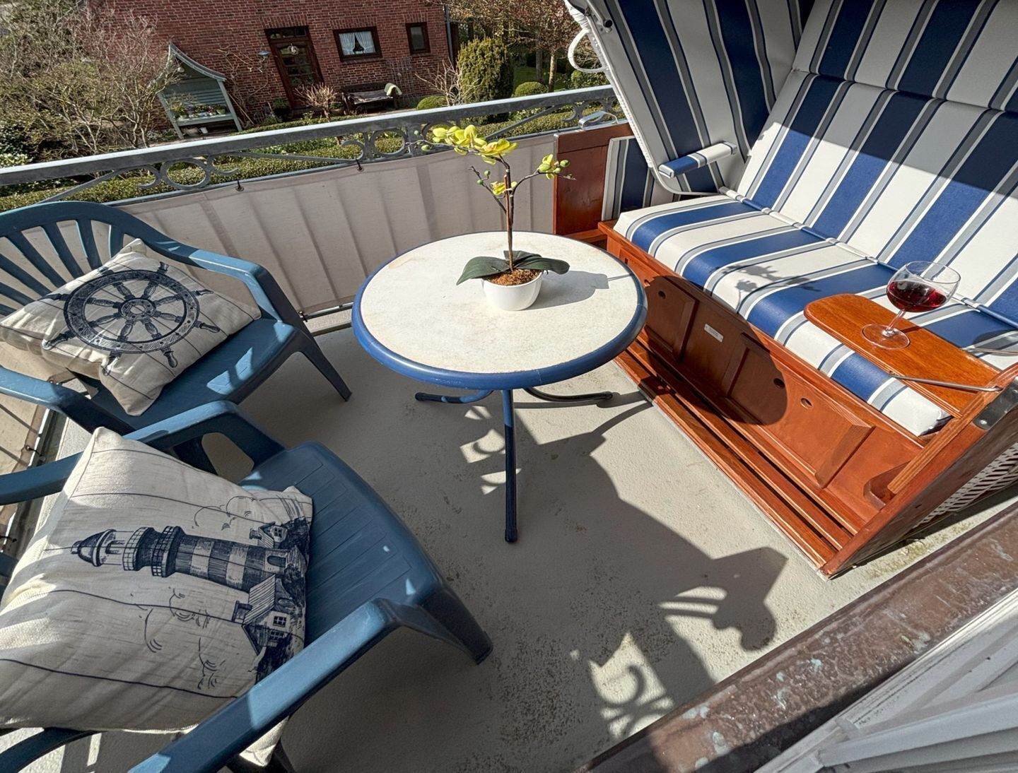 Un balcon avec un canapé à rayures bleues et blanches, une petite table ronde ornée d’une plante, et deux chaises bleues avec des coussins à motifs nautiques.