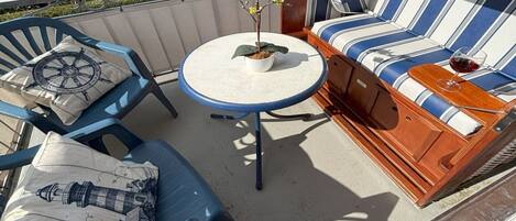 Un balcon avec un canapé à rayures bleues et blanches, une petite table ronde ornée d’une plante, et deux chaises bleues avec des coussins à motifs nautiques.