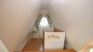 A narrow stairway with a wooden handrail, a white crib with children's drawings, a high chair, and a window with curtains. - Rungholtstraße 6, Whg. 4 - Apartment with 3 rooms on approx. 55m² for max. 2 persons. (Wyk auf Föhr)