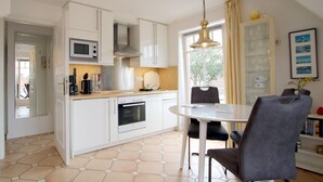 A modern kitchen with white cabinets, a built-in oven, a microwave, and a dining area with a round table and chairs. - Rungholtstraße 6, Whg. 4 - Apartment with 3 rooms on approx. 55m² for max. 2 persons. (Wyk auf Föhr)