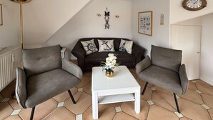 A living room with a sofa, two armchairs, a coffee table, a floor lamp, and a clock on the wall. - Rungholtstraße 6, Whg. 4 - Apartment with 3 rooms on approx. 55m² for max. 2 persons. (Wyk auf Föhr)