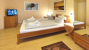 Une chambre d’hôtel avec un grand lit, un téléviseur posé sur une commode en bois et deux tableaux encadrés accrochés au mur.