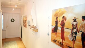 Un couloir doté d’un plancher en bois, une porte ornée d’une guirlande et un tableau représentant trois personnages tenant un parapluie.
