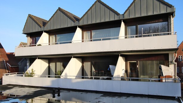 Une maison moderne à deux étages, dotée d’un toit plat, de grandes fenêtres et d’un balcon.