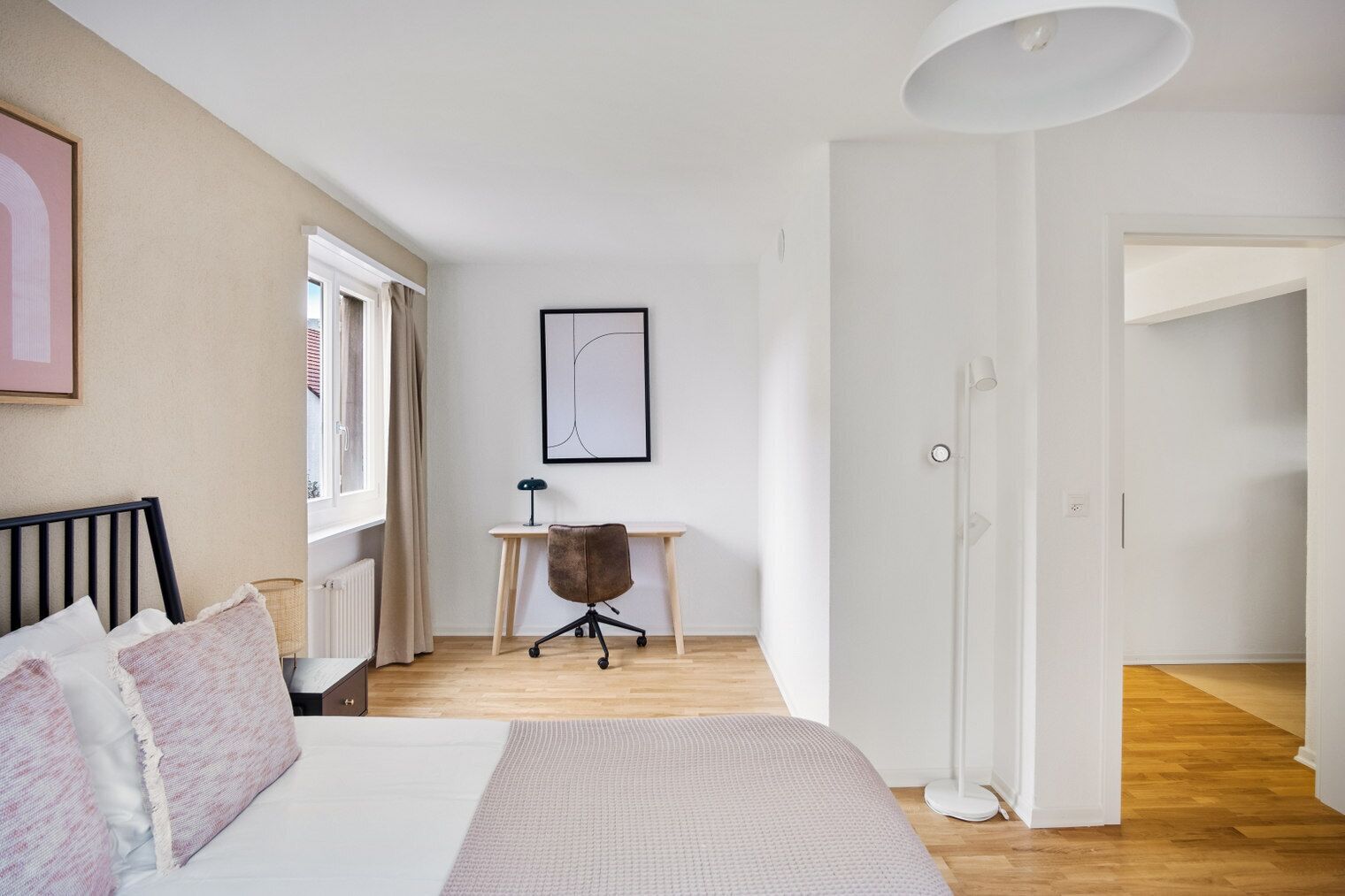 A bedroom with a bed, a desk, a chair, a window with curtains, and a framed picture on the wall.