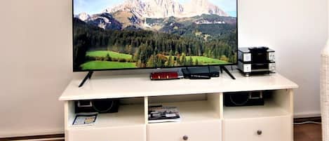 A flat-screen TV on a white entertainment center with two speakers, a remote, and a small book.