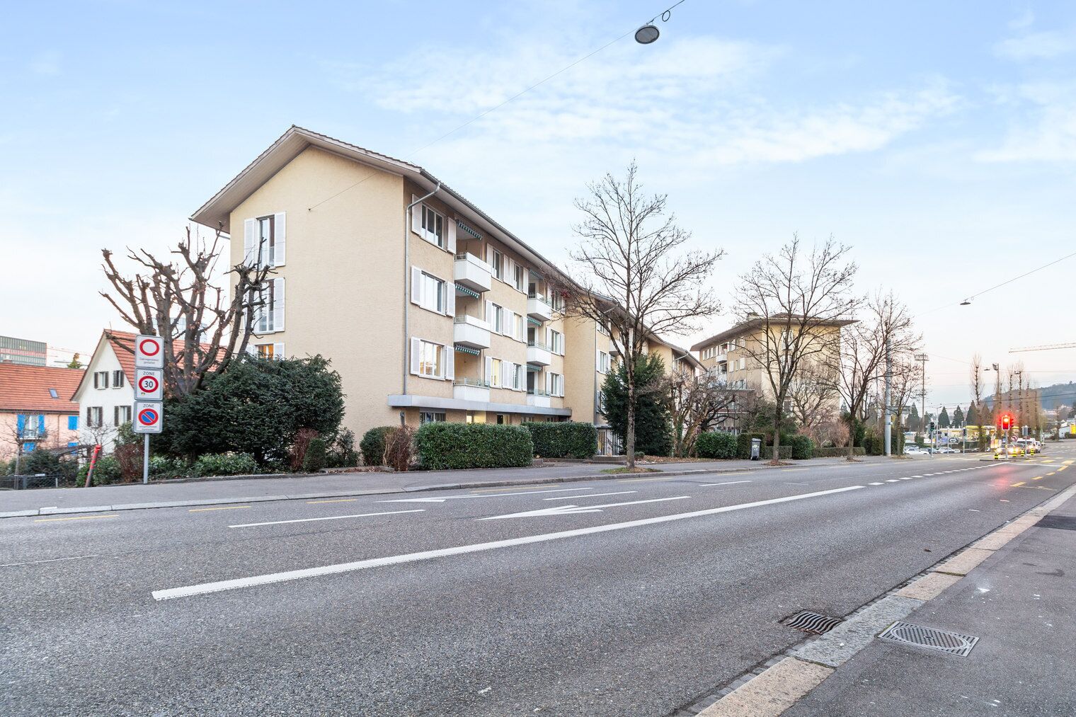 A multi-story residential building with balconies, a clear road in front, and a traffic light in the distance.