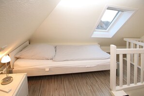 Un dormitorio estilo loft pequeño y blanco con tragaluz, lámpara de noche y cuna blanca.