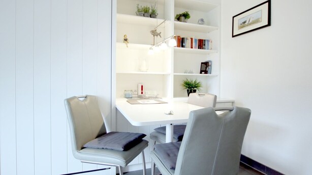 Ein modernes Zimmer mit einem weißen Schreibtisch, zwei Stühlen, einem Bücherregal und einem gerahmten Bild an der Wand.