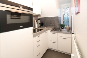 Cocina compacta con microondas, cafetera y un lavamanos pequeño.