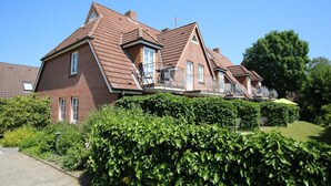 Ein zweigeschossiges Haus mit einem geneigten Dach, einem Balkon mit Metallgeländern und einem gepflegten Garten.
