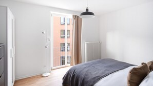 Un dormitorio con cama, radiador, ventana con cortinas y vista a un edificio.