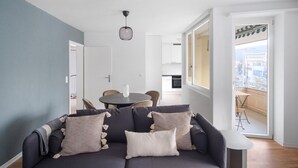 Una sala de estar moderna con un sofá gris oscuro, una mesa de comedor redonda y una cocina al fondo.