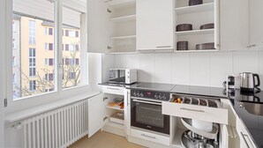 Una cocina moderna con armarios blancos, horno empotrado, microondas y hervidor.