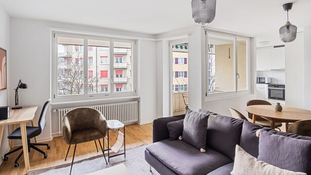 Un apartamento moderno con sofá, mesa de comedor y vista a un edificio con balcones.