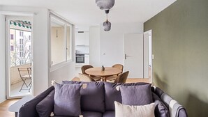 Una sala de estar moderna con un sofá, una mesa de comedor y sillas. Se ve una cocina a través de una puerta abierta.