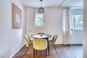 Un comedor con una mesa redonda y cuatro sillas, una lámpara colgante, un cuadro en la pared y una ventana con cortinas.