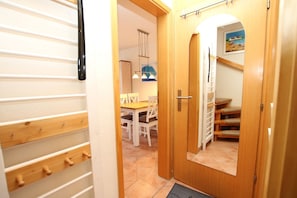 A hallway with a wooden door, a coat rack, and a dining area with chairs and a table.