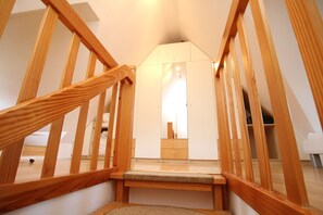 A wooden staircase leading to a bedroom with a bed, a dresser, and a mirror.